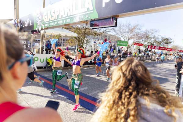 Two mermaid-themed runners crossing the finish line at the Gasparilla Distance Classic